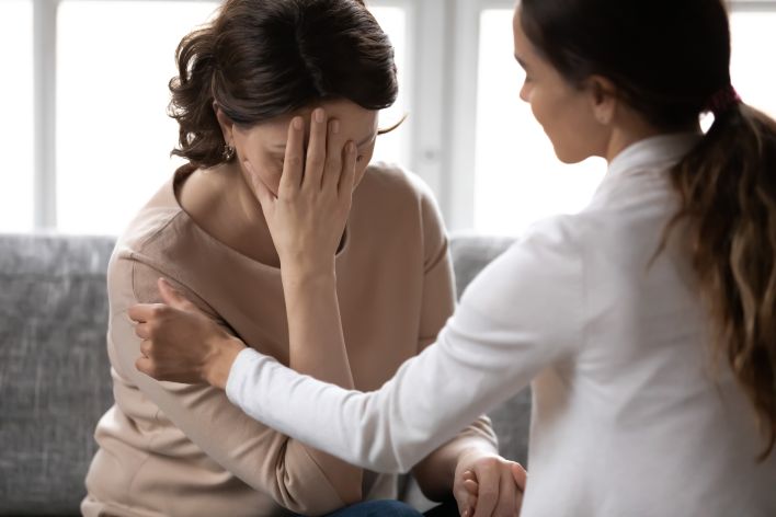 Traumatized woman with hand on face comforted by Psychotherapist